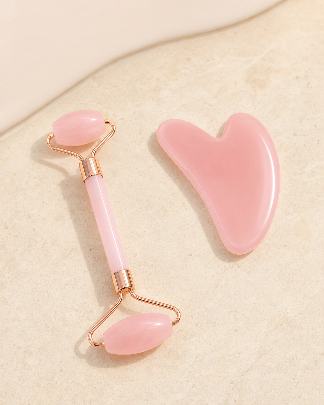 Blush double-ended facial roller and heart-shaped massage board on ivory stone