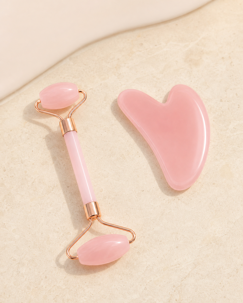 Blush double-ended facial roller and heart-shaped massage board on ivory stone