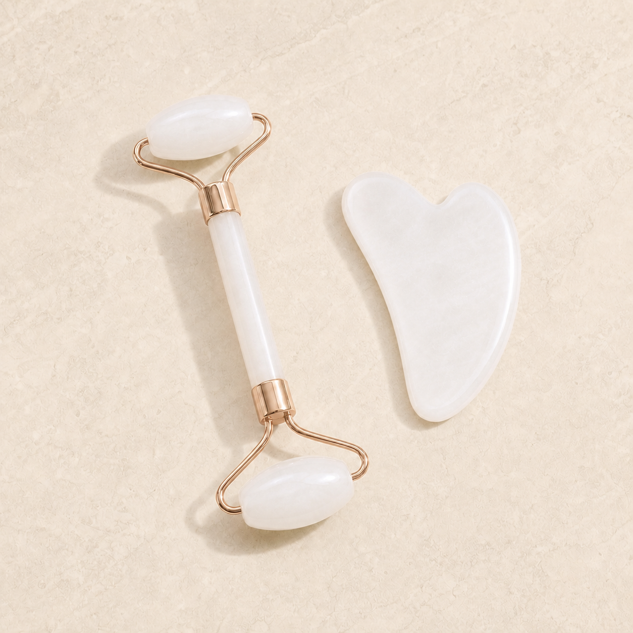 Pearl double-ended facial roller and heart-shaped massage board on ivory stone