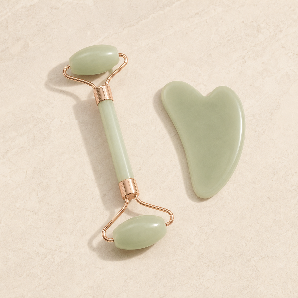 Sage double-ended facial roller and heart-shaped massage board on ivory stone